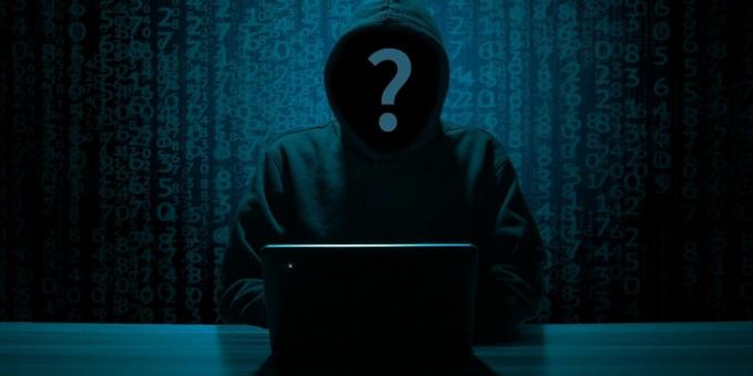 La faccia di un hacker anonimo in una felpa nera con un PC sul tavolo