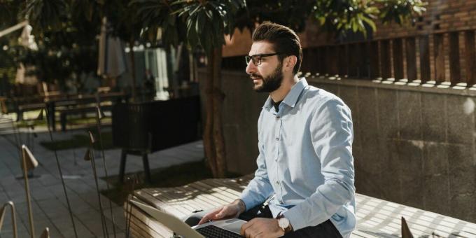 Un uomo con un laptop seduto su una panchina nel parco