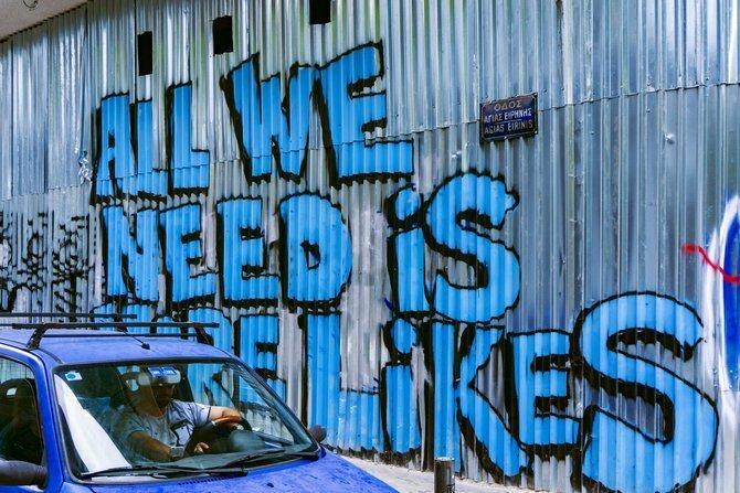 Auto accanto a un muro di graffiti che recita "All We Need Is More Likes"