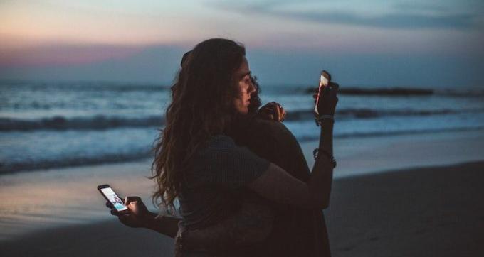 Una coppia che abbraccia e guarda i loro telefoni sulla spiaggia