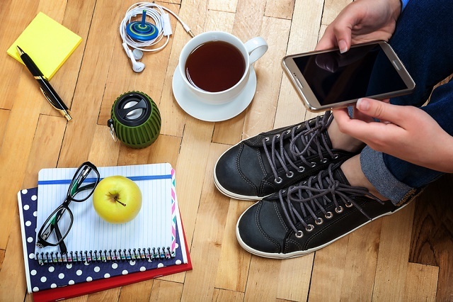 Persona con smartphone, tazza di caffè, taccuino ecc.