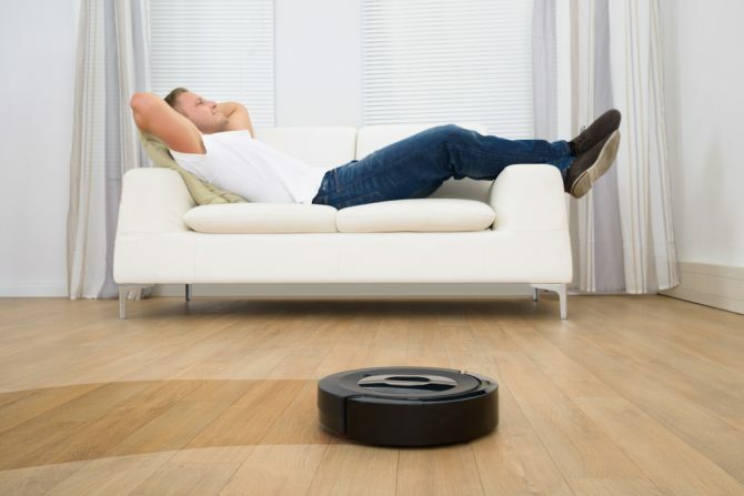 Uomo che si rilassa su Sofa With Robotic Aspirapolvere sul pavimento di legno duro